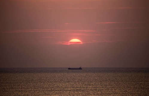 Cargo ship in the Mediterranean Sea under the evening sun, photographed from the beach near