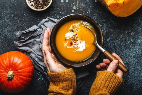 Woman in yellow knitted sweater eating a pumpkin cream soup on dark stone background with spoon