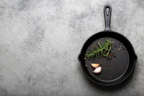 Black cast iron frying pan with ingredients for cooking: fresh green rosemary, raw garlic cloves