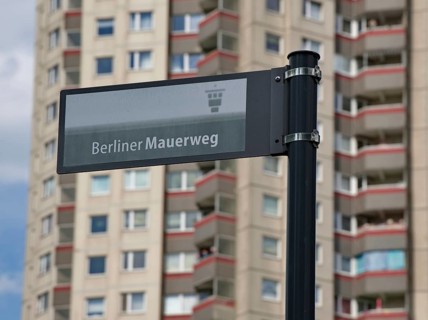 Sign with the inscription Berliner Mauerweg in front of a high-rise building in Gropiusstadt,