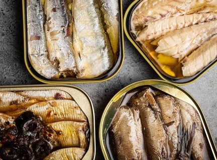 Assorted canned fish in a tin over gray concrete background: sardine, smoked sardine, mackerel.