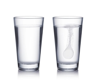 Glass with effervescent tablet in water with bubbles on white background