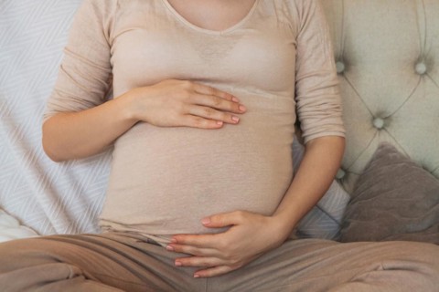 Cropped shot of pregnant woman holding belly while relaxing on couch at home, expectant mother