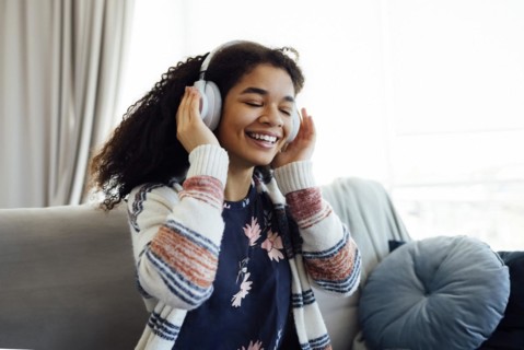 African millennial woman in orange sweater wearing white wireless headphones, listening music,