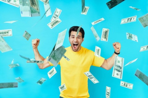 Happy excited man standing under money rain banknotes falling down. Success, business, and fortune