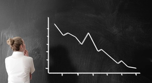 rear view of businesswoman looking at chart with sloping curve, dropping prices business risk