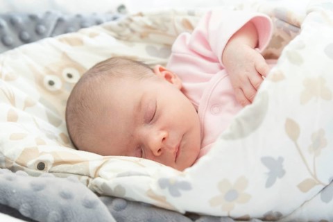 Sleeping newborn baby. Cute little girl one week old at home. Adorable lying on side covered with