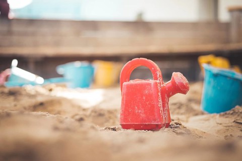 Children plastic toys in the sand box. Watering can, selective focus