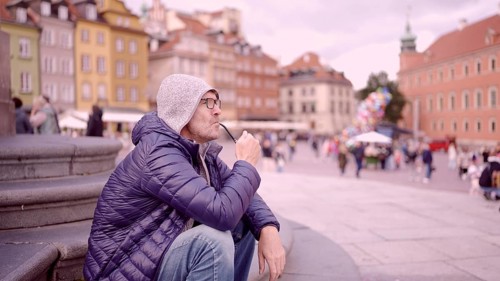 Portrait of adult man with glasses sitting in the hood on square and smoking a tobacco pipe in the