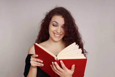 smiling teenage girl enjoys reading a funny hardcover book