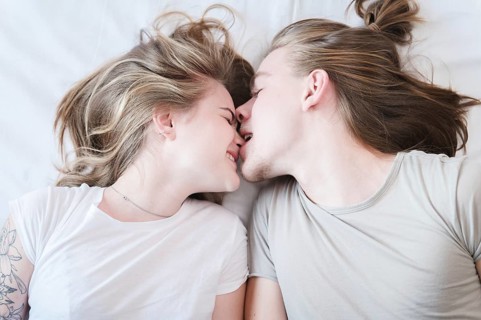 A top view of a molo pair of long-haired men and women laughing around fooling around in bed. A man