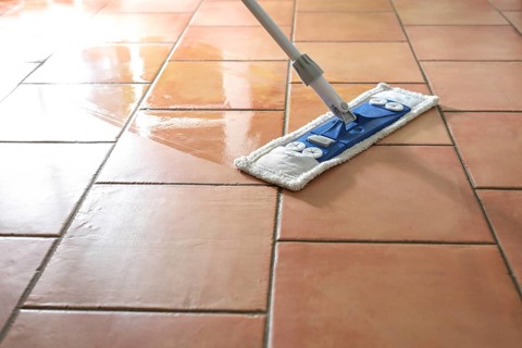 Flat wet-mop made of microfiber wipes the tiled terracotta floor, daily cleaning routine for a