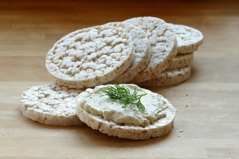 Group of rice cakes, one with cream cheese and herbs on a wooden board