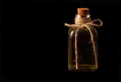 Close-up of a glass bottle with olive oil and cork stopper isolated on a black background