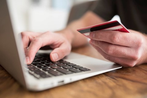 online shopping concept, person entering payment information on laptop computer holding debit or