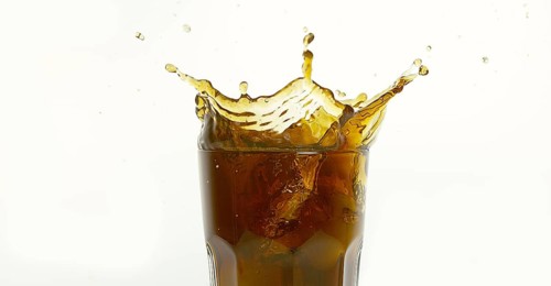 Ice Cubes Falling into Glass of Coke against White Background