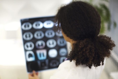 Rearview of ethnic female doctor analyzing X-ray or MRI scan while working in hospital, selective