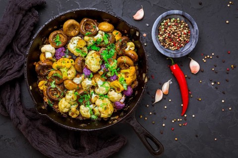 Roasted mushrooms and cauliflower, with onion, garlic and herbs in pan on black background