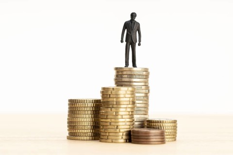 Wealth, making money, wage growth concept. Businessman figurine standing on a pile of coins. Copy