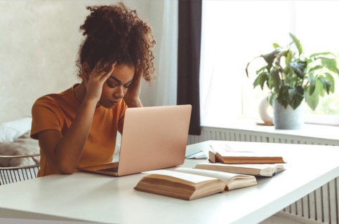 Tired flustrated African descent young girl sitting at desk in front of laptop while irritably