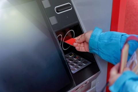Woman in blue jacket inserting her credit card into an ATM to withdraw cash