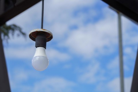 Light bulb hanging from a wire with a rusty lamp over a blue sky with clouds