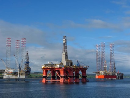 Three oil rigs standing side by side in a calm sea under a blue sky, partly cloudy, drilling rigs