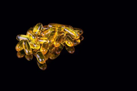 Capsules with fish oil on black background with reflection and copyspace
