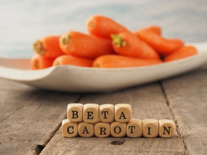 Wooden dices with the German words beta carotene and fresh carrots in the back, healthy eating