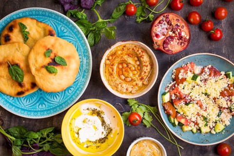 Table served with middle eastern traditional vegetarian dishes. Hummus, tahini, pitta, couscous