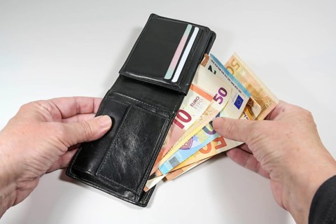 Hands taking various euro banknotes out of a black leather wallet, money and finance concept, light