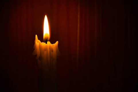 Single yellow wax candle burning alone in the dark red background. Conceptual image symbolize