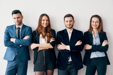 Young smiling business people with arms crossed lean to wall in office. Success teamwork concept
