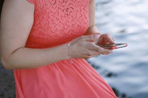 unrecognizable young woman sitting by the water using her smartphone or mobile phone