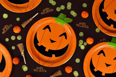 Halloween party flat lay with orange pumpkin paper plates, witch brooms, confetti and Happy