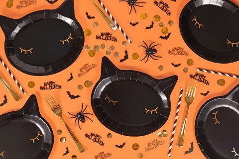 Black cat shaped Halloween party paper plates, bats and Happy Halloween text confetti on orange