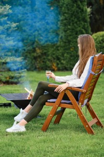 Young woman resting in lounge chair on backyard next to a barbecue, view on profile