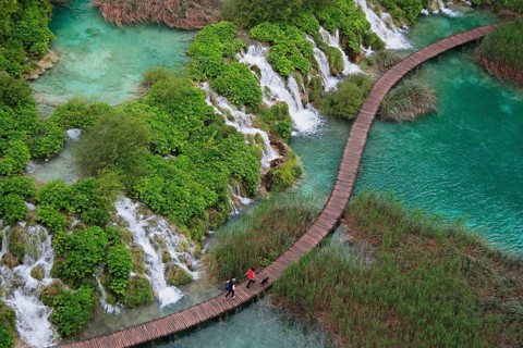 Wooden footbridge with hikers over turquoise ponds and waterfalls at Plitvice Lakes, Croatia,
