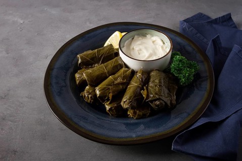 Dolma, cabbage rolls, grape leaves with filling, white sauce, lemon and herbs, rustic, selective