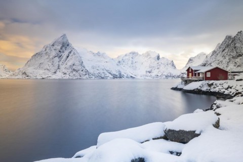 Red huts on the island of Sakrisøy, snow-covered mountains in the background, Sakrisoy, Reine,