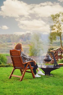 Unrecognizable young woman rests near fireplace at backyard in her country house