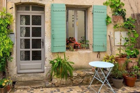 An old house façade with green shutters, numerous plants and a small round table, Vauvenargues,