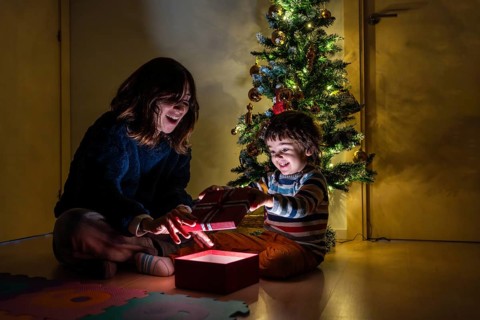 A woman and a child are opening a present in front of a Christmas tree. Scene is joyful and