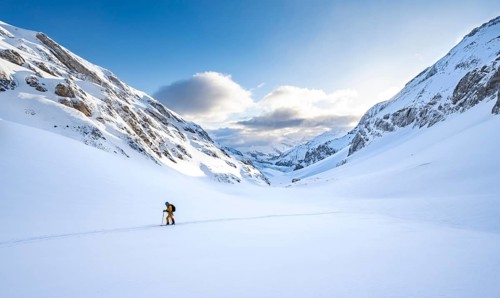 Ski tourers ascending through untouched fresh snow, snow-covered mountain landscape with blue sky