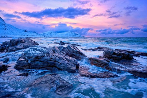Waves of Norwegian sea on rocky coast in fjord on sunset with sun. Skagsanden beach, Lofoten