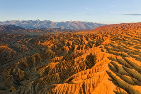 River bed runs through a landscape of eroded hills, badlands at sunset, mountain peaks of the Tian