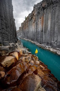 Tourist standing by the river in Stuðlagil Canyon, turquoise blue river between basalt columns,