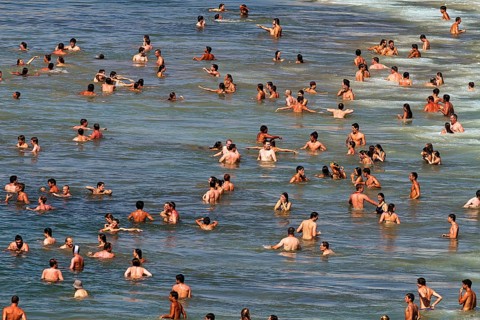 View from above on crowd on the beach, tourists swimming in the sea, enjoying cooling off, fun,