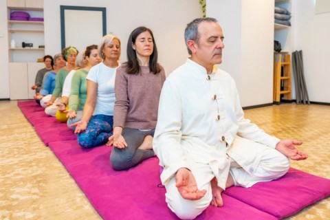 Yoga teacher leading a meditation in a community sitting on mat with lotus position