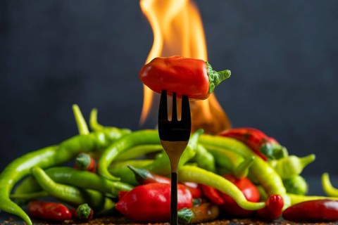 A red pepperoni on a fork, pepperoni and fire in the background, food photography